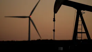 A pumpjack operates in the foreground while a wind turbine at the Buckeye Wind Energy wind farm rises in the distance, Sept. 30, 2024, near Hays, Kan. (AP Photo/Charlie Riedel, File)