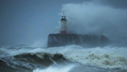 A lighthouse, battered by waves, sits at the center of this dark and stormy seascape.