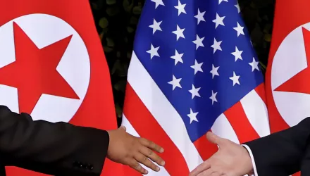 two hands reaching to shake in front of U.S. and North Korean flags.