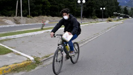 A man wearing a mask rides a bicycle on a street in Epuyen, Argentina, Friday, Jan. 11, 2019. An Argentine judge has ordered 85 residents of a remote Patagonian town to stay in their homes for at least 30 days to help halt an outbreak of hantavirus in which nine people have died. (AP Photo/Gustavo Zaninelli)