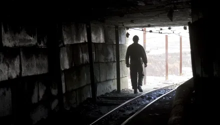 A miner is silhouetted at the mouth of a dark mine tunnel.