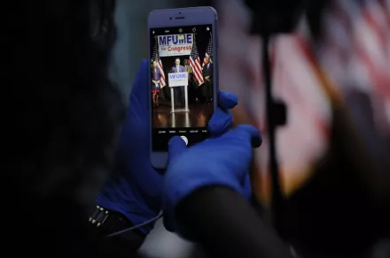 A staff member in the Kweisi Mfume campaign uses gloves while holding a cell phone during an election night news conference at his campaign headquarters after Mfume, a Democrat, won Maryland’s 7th Congressional District special election, Tuesday, April 28, 2020, in Baltimore.
