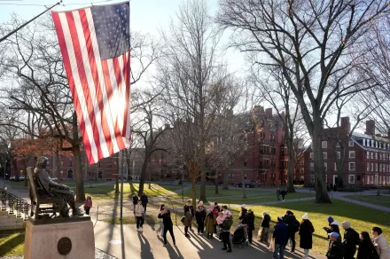 People take photographs near a John Harvard statue