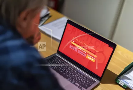 A man sits in an office in front of a laptop that is infected with a fictitious encryption Trojan (ransomware). 