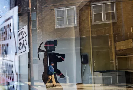 A mural of a coal miner stands in an empty storefront as signs advertising vacant apartments and stores hang in the windows along the main business street in Cumberland, Ky.