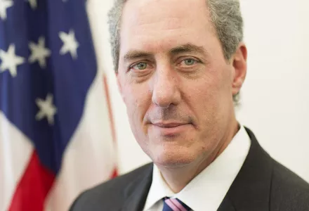 Ambassador Michael Froman stands in front of an American Flag