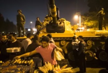 A street vendor grills corn as Egyptian soldiers stand guard and as protestors opposing President Mohammed Morsi gather during a demonstration at the Presidential Palace on December 18, 2012 in Cairo, Egypt.