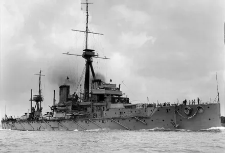HMS Dreadnought underway, with an anchor suspended from the starboard deck edge, circa 1906–1907. Note the array of booms used to deploy her anti-torpedo net system.