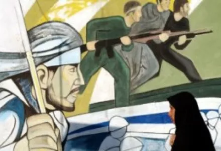A veiled Iranian woman walks past a revolutionary mural including images commemorating the 1980–1988 Iran-Iraq War in Tehran, Iran, July 1, 2004.