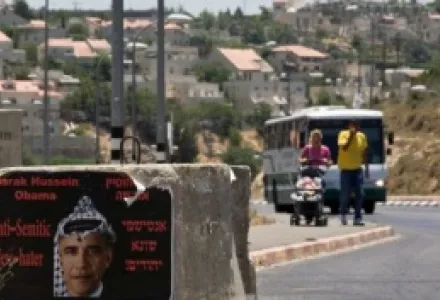 A couple walks next to sign hung by an extremist right wing group depicting U.S. President Barack Obama, next to the settlement of Efrat, seen in the background, in the West Bank, June 19, 2009.