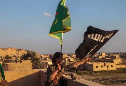 A YPJ fighter replaces the ISIS flag with one from the all-female force in Baghuz, Syria. The YPJ and YPG are core components of the Syrian Democratic Forces.
