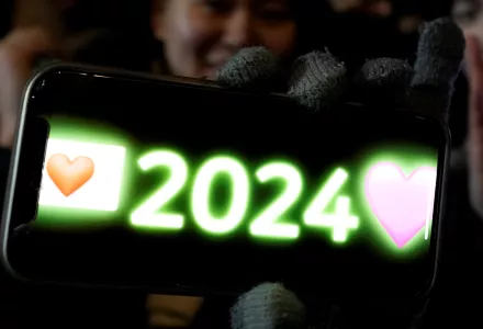 A woman poses for a photo with her smartphone displaying 2024