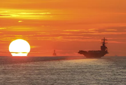 As the setting sun looms large across the South China Sea, it silhouettes an aircraft carrier in the foreground and other U.S. Navy ships in the distance.