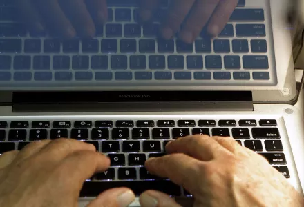Close-up of two hands placed on the laptop keyboards with reflection on the screen.