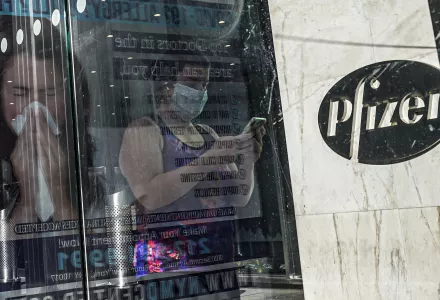 In this Nov. 9, 2020, file photo, an ad for COVID-19 testing reflects on glass at a bus stop, as pedestrians walk past Pfizer world headquarters in New York. 