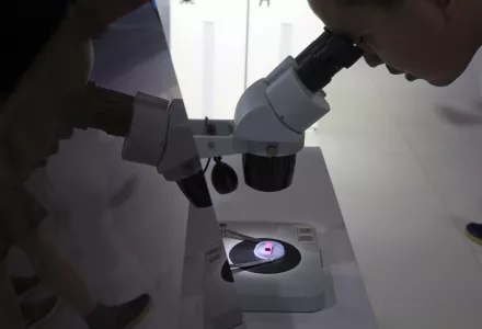 In this file photo taken Thursday, May 17, 2018, a visitor to the 21st China Beijing International High-tech Expo looks at a computer chip through the microscope displayed by the state-controlled Tsinghua Unigroup project which has emerged as a national champion for Beijing's semiconductor ambitions in Beijing, China. 