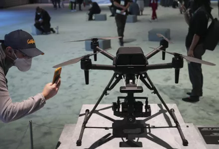 A person on the left bends to take pictures of a drone showcased on a platform on the right.