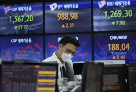 A currency trader sits in front of screens showing numbers of multiple national currencies.