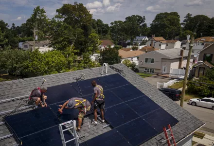 three workers install solar panels on roof of home