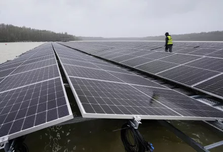 Man in hardhat walks between floating solar panels on a lake