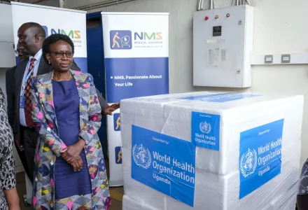 Uganda's Minister of Health stands next to a box of vaccine labeled with World Health Organization Uganda on it