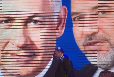 Israeli Foreign Minister Avigdor Lieberman walks under a screen showing him and Israeli Prime Minister Benjamin Netanyahu during the inauguration of their election campaign in Jerusalem, Dec. 25, 2012.