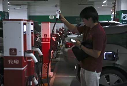 A man prepares to charge his electric-powered vehicle parked at a shopping mall in Beijing, Monday, Sept. 11, 2017. 