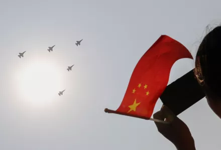A woman holding a flag films PLA Air Force jets as they fly in formation during a parade to commemorate the 70th anniversary of the founding of the People’s Republic of China in Beijing, Tuesday, Oct. 1, 2019.