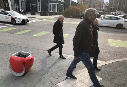 Photo of man crossing street in Boston followed by his Gita carrier robot carrying a backpack. 