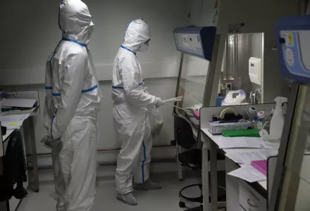 French lab scientists in hazmat gear inserting liquid in test tube manipulate potentially infected patient samples at Pasteur Institute in Paris