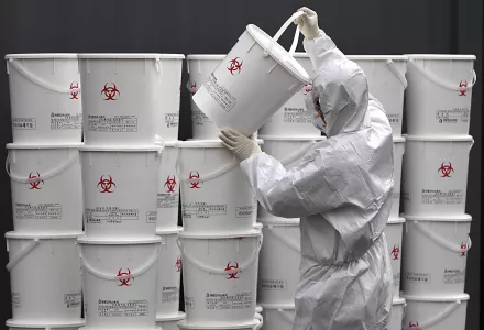 A worker in protective gear stacks plastic buckets containing medical waste from coronavirus patients at a medical center in Daegu, South Korea, Monday, Feb. 24, 2020. 