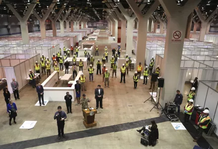 llinois Gov. J.B. Pritzker, lower center, and Chicago Mayor Lori Lightfoot, with hands behind back, to left of Pritzker in photo, listen during a news conference in Hall C Unit 1 of the COVID-19 alternate site at McCormick Place in Chicago on Friday, April 3, 2020.