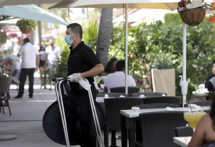 In this July 12, 2020, file photo, a waiter wears a protective face mask and gloves while working at the il bolognese restaurant along Ocean Drive during the coronavirus pandemic, in Miami Beach, Fla. Unemployment remains painfully high in the U.S. even as economic activity is slowly picking up.