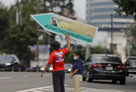 John Miller, 25, of Atlanta, spins a large check sign for the #OneCheckIsNotEnough campaign near Georgia Sen. David Perdue's office on Tuesday, Aug. 11, 2020, in Atlanta. 