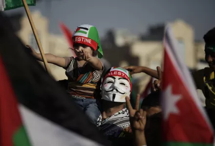 A man wears a Guy Fawkes mask and carries his daughter during a celebration by the Muslim Brotherhood movement to declare victory of Gaza and Hamas against Israel, in Amman, Jordan, Friday, Aug. 29, 2014. (AP Photo/Mohammad Hannon)