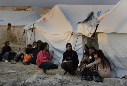 Displaced Syrians wait outside tents.