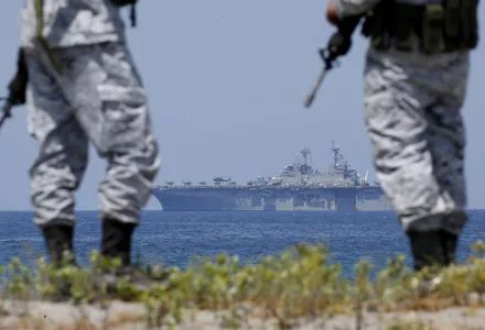 Solider stand on shore with naval ship in the distance