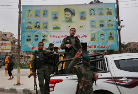 In this photo taken on Wednesday, March 28, 2018, members of the Kurdish internal security forces stand on their vehicle in front of a giant poster showing portraits of fighters killed fighting against the Islamic State group, in Manbij, north Syria. Manbij, a mixed Arab and Kurdish town of nearly 400,000, was liberated from Islamic State militants in 2016 by the YPG fighters with backing from U.S-led coalition airstrikes. With Turkey's threats, the town has become the axle for U.S. policy in Syria, threate