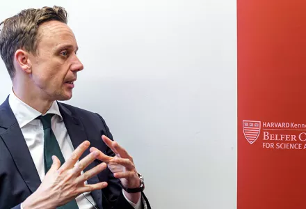 John Bew on the left and a crimson banner with the Belfer Center word mark on the right.
