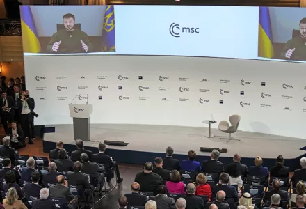 A wide shot of a crowd watching two large video screen with Ukraine President Zelenskyy on them at the Munich Security Conference