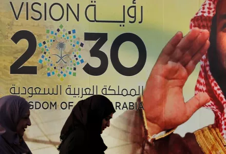 Women walking in front of Saudi Vision 2030 poster.