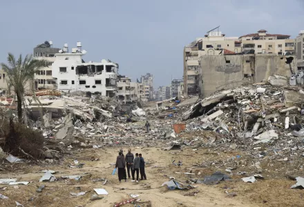 Palestinians walk past the building destroyed in the Israeli Bombardment of Gaza (AP Photo/Mohammed Hajjar)
