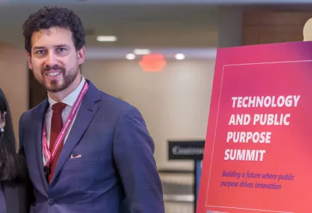 Two people stand next to a sign that says Technology and Public Purpose Summit