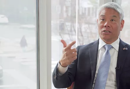 John Tien speaking in front of a window with Harvard Square in the background
