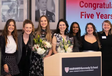 Women line up in front of a screen reading "congratulations on five years at HKS"
