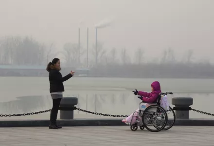 Visitors in a park gesture at each other near chimneys spewing smoke in Beijing, China