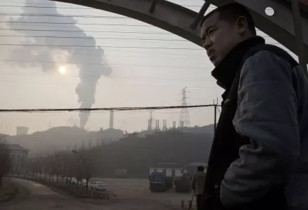 a man looks up near smoke spewing from a chimney near the Jiujiang steel and rolling mills in Qianan