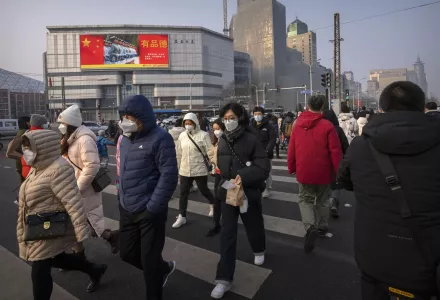 Commuters wearing face masks walk across an intersection near an electronic billboard for China's armed forces during the morning rush hour in Beijing, Friday, Feb. 10, 2023. 