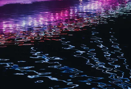 Neon lights reflect off rippling water.