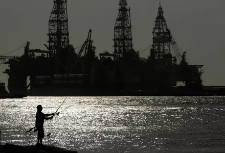 A man fishes near an oil drilling platform 